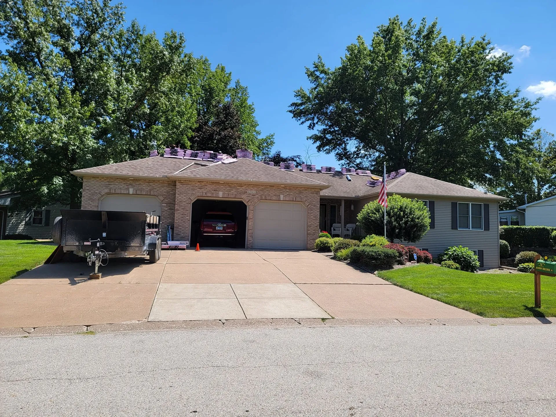 Ranch home mid roof replacement with shingle bundles on the roof and a dump trailer