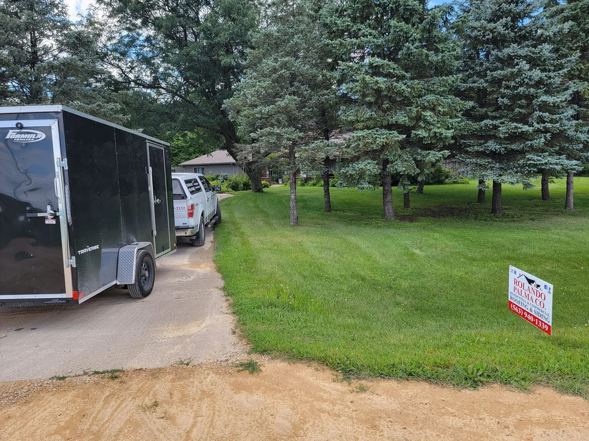 Roofing trailer and pickup truck at a job site with a Rolando Palma Co. yard sign