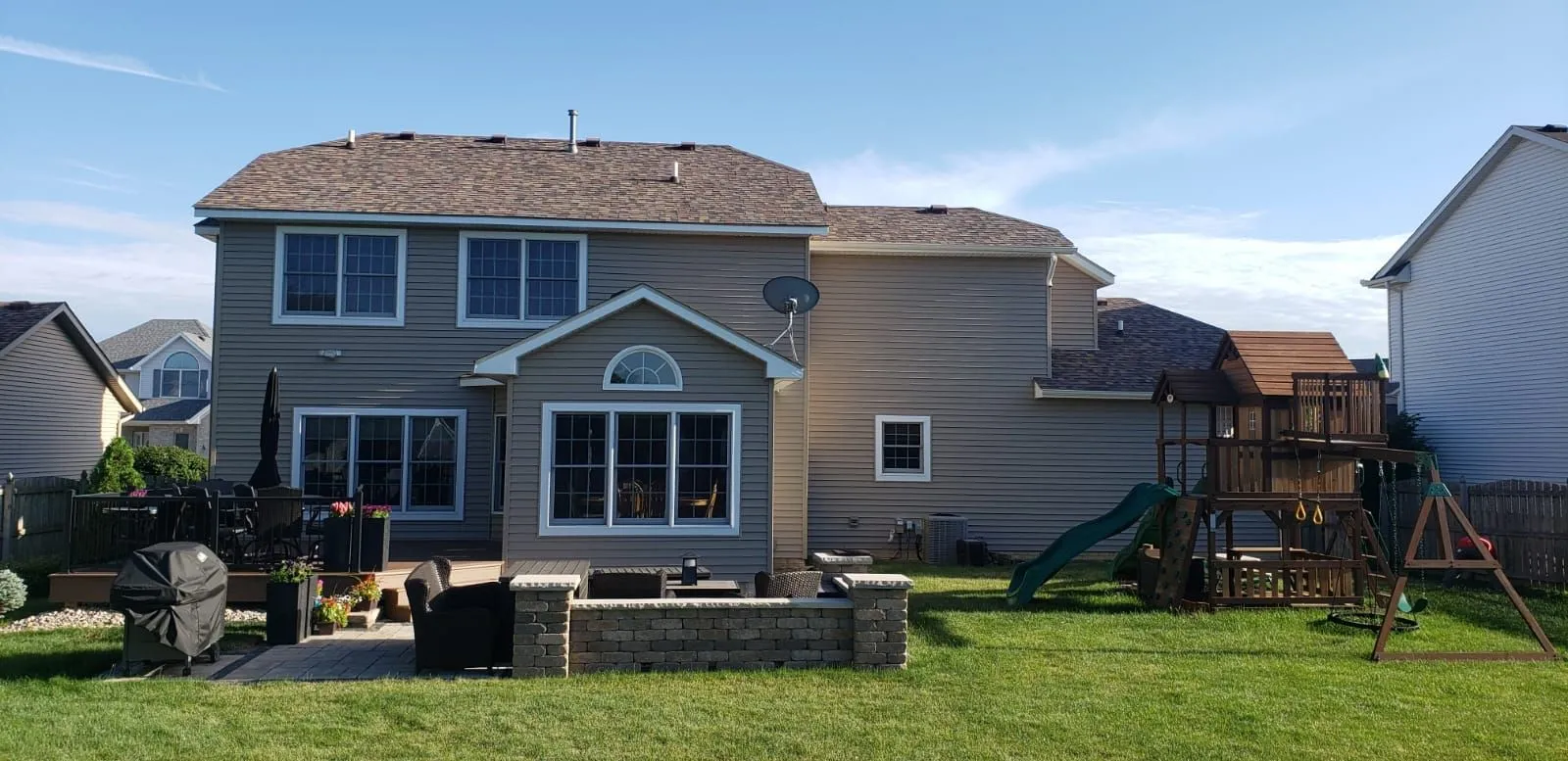 Back of a two-story home with a new roof, patio and backyard playset