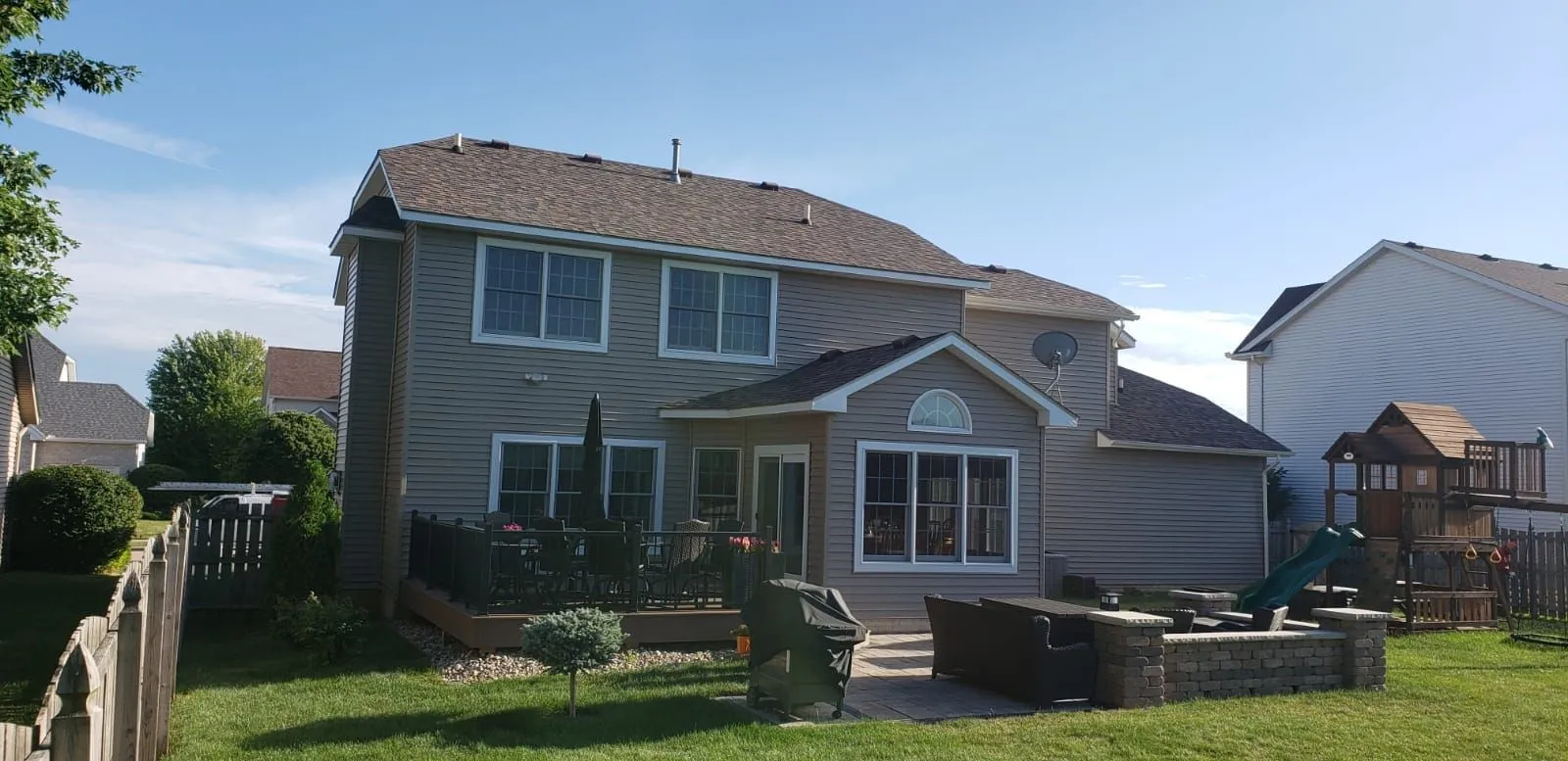 Two-story home with a finished shingle roof seen across the backyard lawn