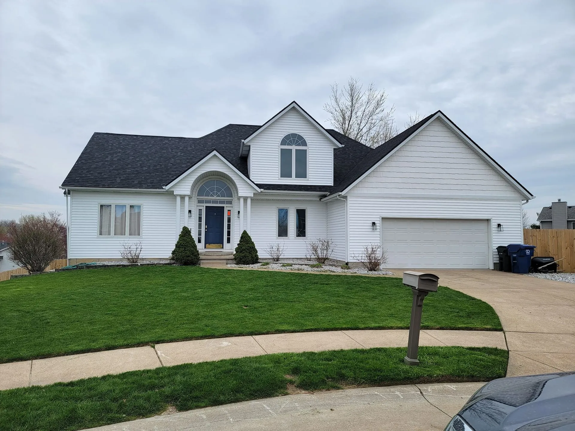 White home with a black shingle roof, arched window and front lawn